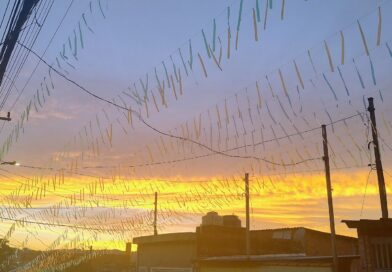 Sunset over a neighborhood with many pastel ribbons strung on wires between utility poles and rooftops.