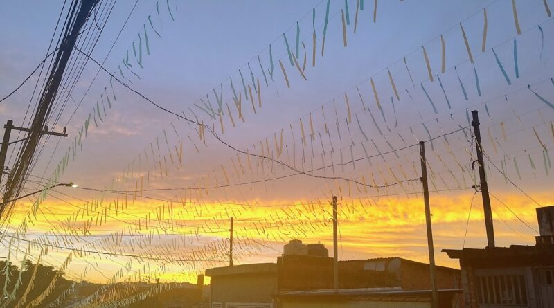 Sunset over a neighborhood with many pastel ribbons strung on wires between utility poles and rooftops.