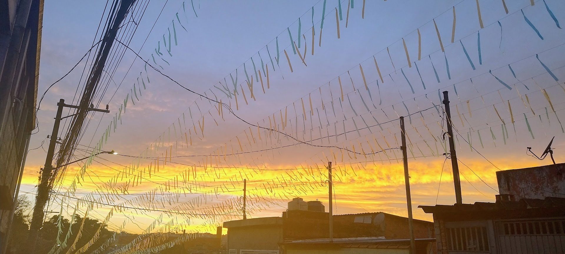 Sunset over a neighborhood with many pastel ribbons strung on wires between utility poles and rooftops.