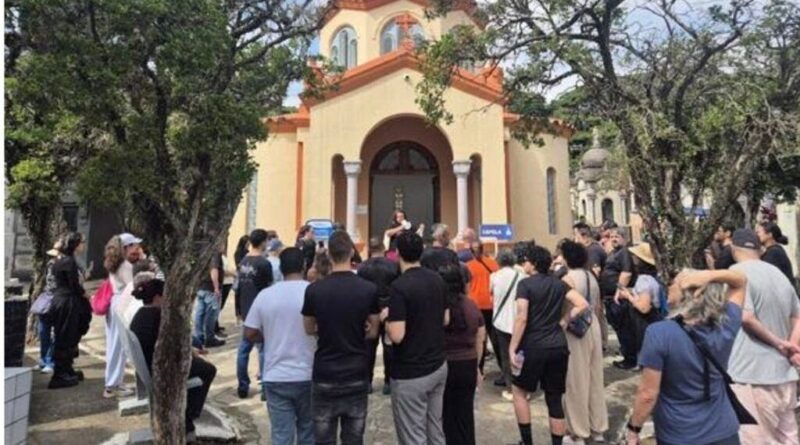 Crowd gathered outside a yellow church with arched doorway and columns, listening to a speaker at the entrance.