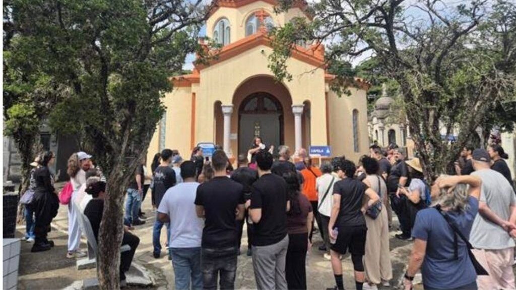 Crowd gathered outside a yellow church with arched doorway and columns, listening to a speaker at the entrance.